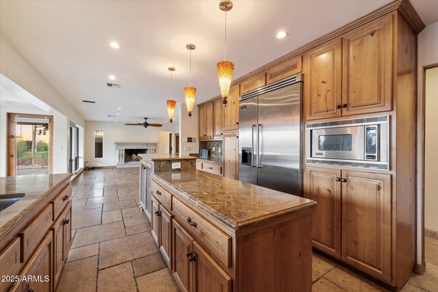 kitchen featuring built in appliances, stone tile flooring, a kitchen island, open floor plan, and dark stone counters