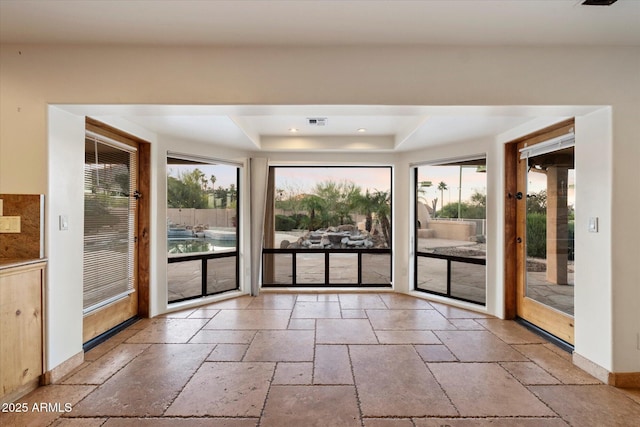 doorway to outside with stone tile floors, a raised ceiling, healthy amount of natural light, and baseboards