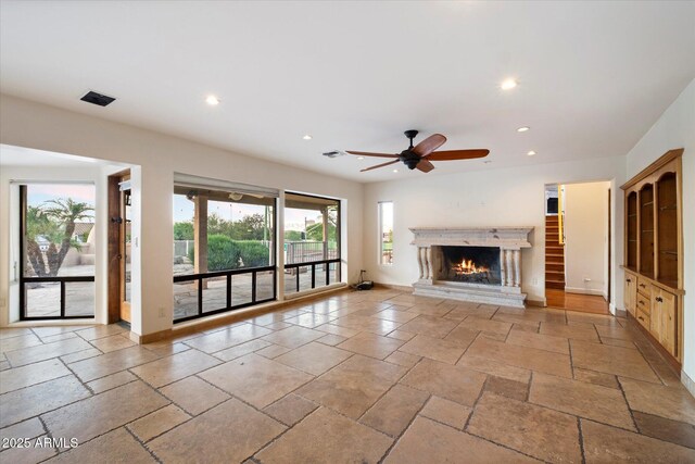 unfurnished living room with recessed lighting, a ceiling fan, stone tile floors, a warm lit fireplace, and baseboards