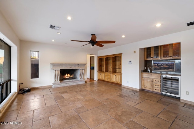 unfurnished living room with beverage cooler, stone tile floors, a warm lit fireplace, recessed lighting, and bar area