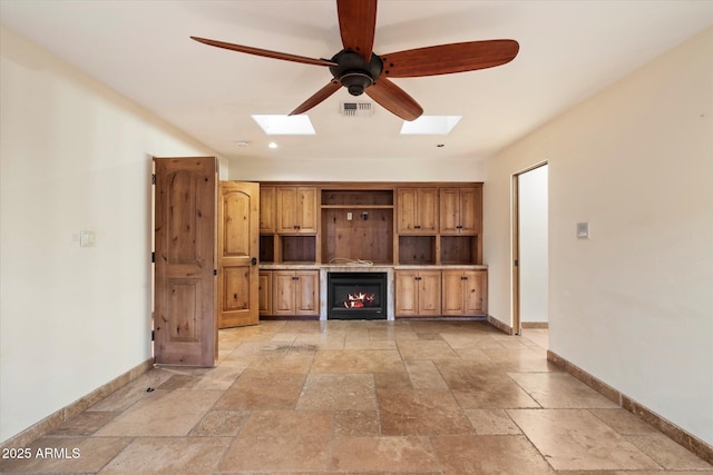 unfurnished living room with a skylight, ceiling fan, baseboards, and stone tile floors