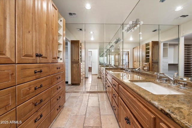 bathroom featuring stone tile flooring, double vanity, and recessed lighting