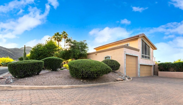 view of side of property with stucco siding, a mountain view, driveway, and a garage