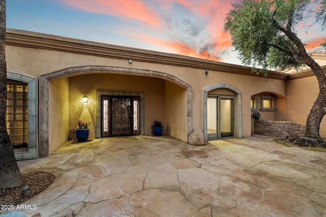 exterior entry at dusk with a patio area and stucco siding