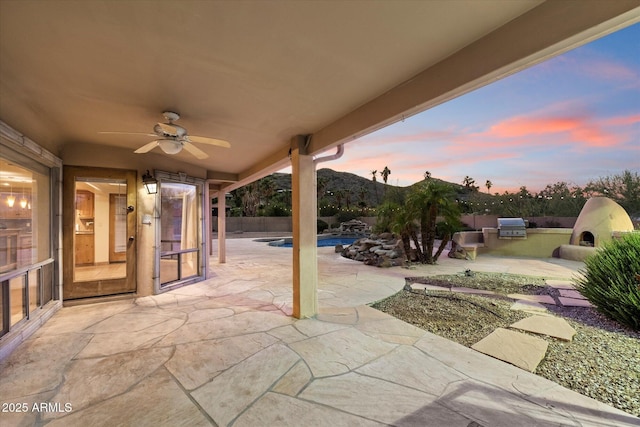 patio terrace at dusk featuring exterior kitchen, ceiling fan, and a fenced backyard