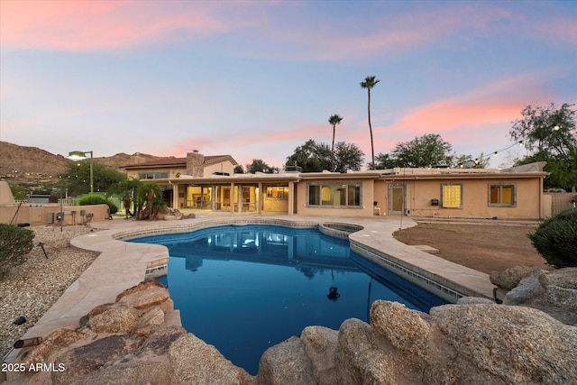 pool at dusk with a patio area, an outdoor pool, and a jacuzzi