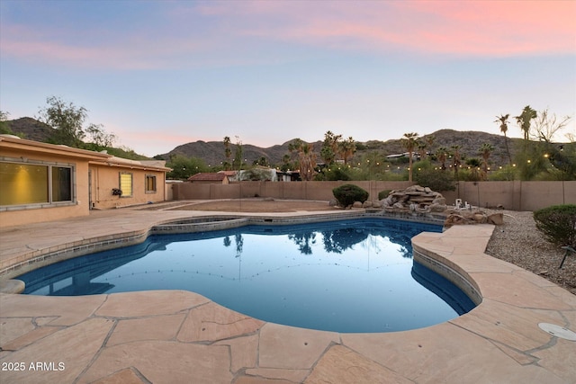 pool at dusk with a mountain view, a fenced backyard, a patio area, and a pool with connected hot tub