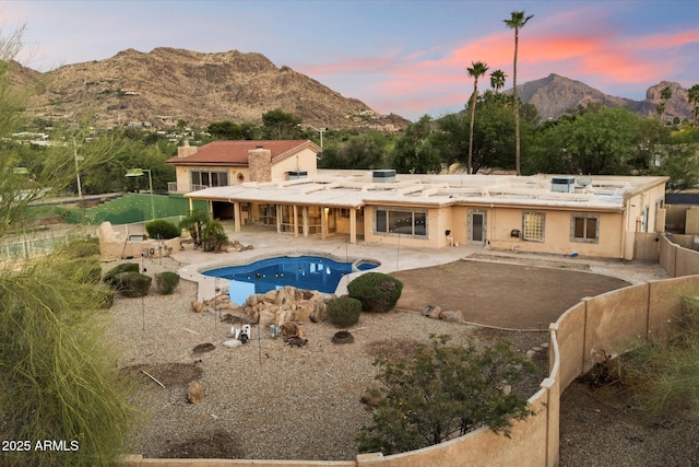 back of house at dusk with a patio, a chimney, a mountain view, a fenced backyard, and an outdoor pool