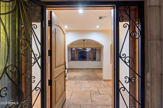 hall with stone tile floors, arched walkways, recessed lighting, and baseboards