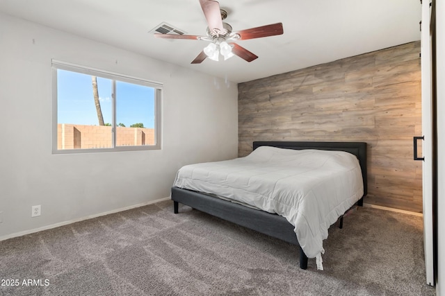 carpeted bedroom featuring ceiling fan and wood walls