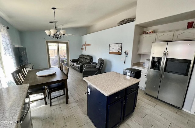 kitchen featuring lofted ceiling, stainless steel fridge, a kitchen island, pendant lighting, and white cabinets