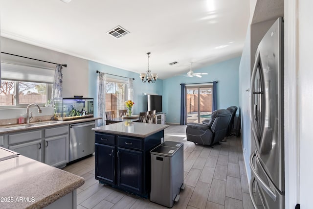 kitchen featuring sink, ceiling fan with notable chandelier, stainless steel appliances, a kitchen island, and decorative light fixtures