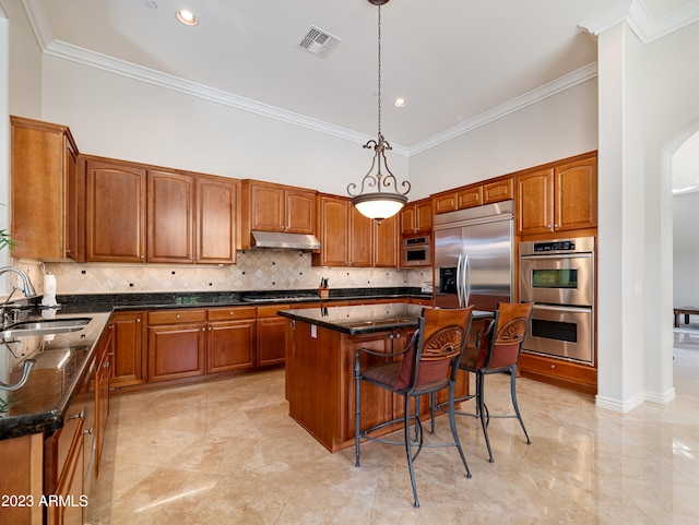 kitchen featuring brown cabinetry, a breakfast bar, stainless steel appliances, under cabinet range hood, and a sink