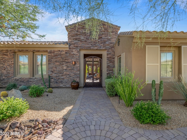 property entrance with stone siding, a tile roof, french doors, and stucco siding