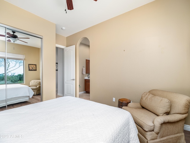 bedroom with a ceiling fan, arched walkways, a closet, and wood finished floors