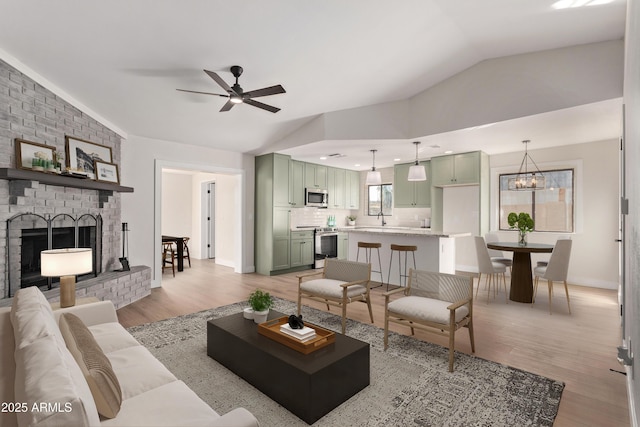 living room featuring a fireplace, ceiling fan with notable chandelier, light hardwood / wood-style floors, and vaulted ceiling