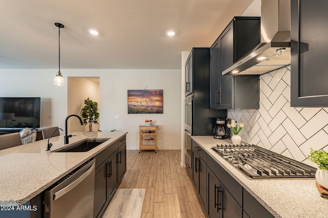 kitchen with light wood finished floors, tasteful backsplash, stainless steel appliances, wall chimney range hood, and a sink