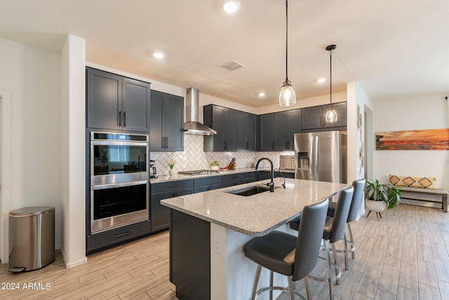 kitchen with visible vents, appliances with stainless steel finishes, light stone counters, wall chimney range hood, and a sink