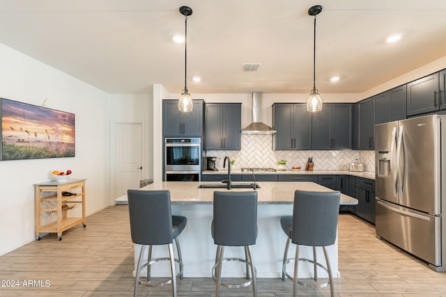 kitchen with visible vents, appliances with stainless steel finishes, light wood-style floors, a sink, and wall chimney exhaust hood