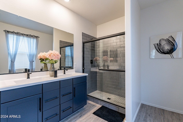 bathroom with a sink, double vanity, a stall shower, and wood finished floors