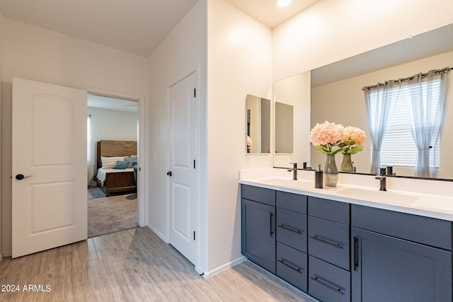 ensuite bathroom with double vanity, connected bathroom, a sink, and wood finished floors