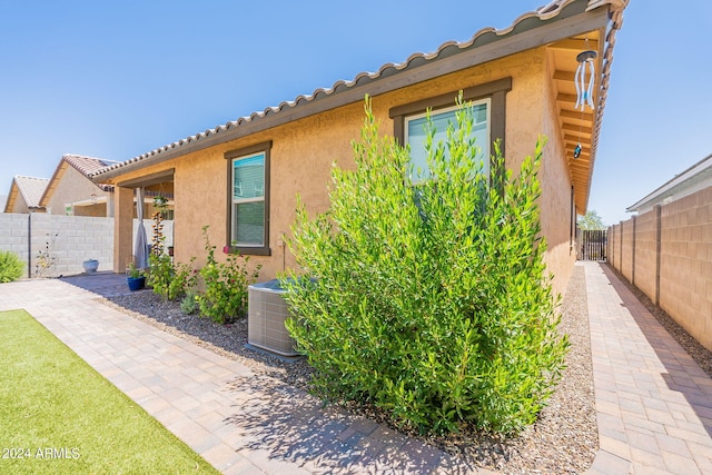 view of property exterior with a tiled roof, cooling unit, fence private yard, and stucco siding