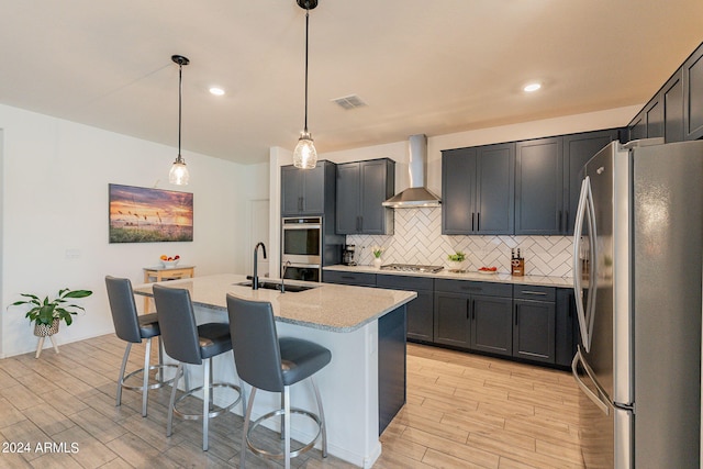 kitchen with visible vents, decorative backsplash, appliances with stainless steel finishes, a sink, and wall chimney range hood