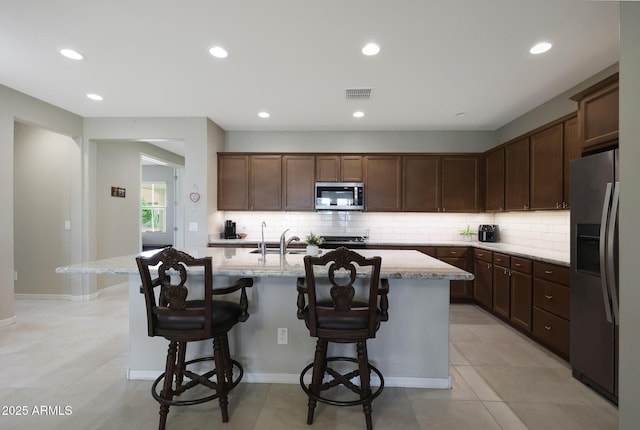 kitchen with a kitchen breakfast bar, visible vents, appliances with stainless steel finishes, a center island with sink, and backsplash