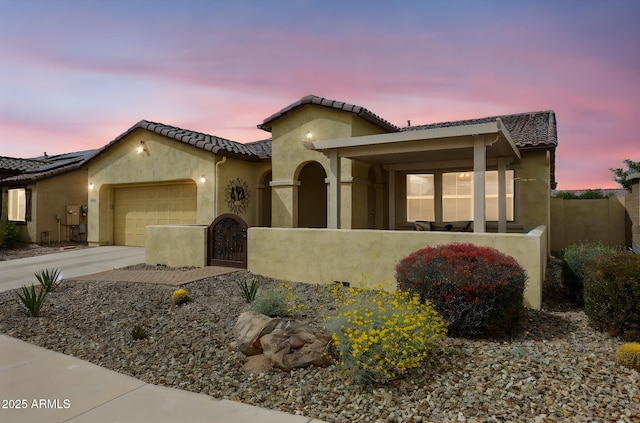mediterranean / spanish-style house featuring stucco siding, fence, an attached garage, and a tile roof