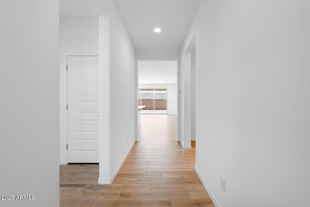 corridor featuring baseboards, recessed lighting, and light wood-style floors