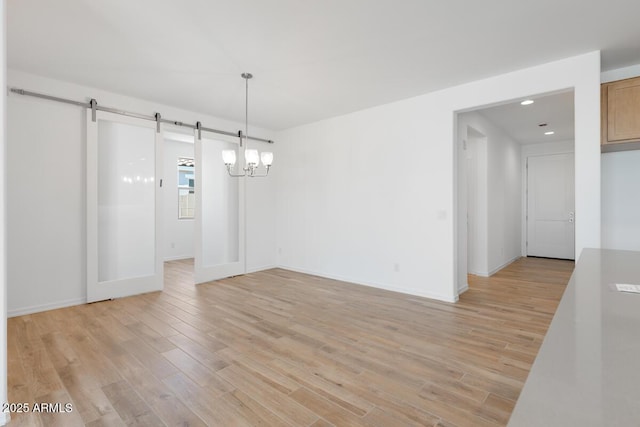unfurnished dining area with a barn door, light wood-style floors, baseboards, a notable chandelier, and recessed lighting