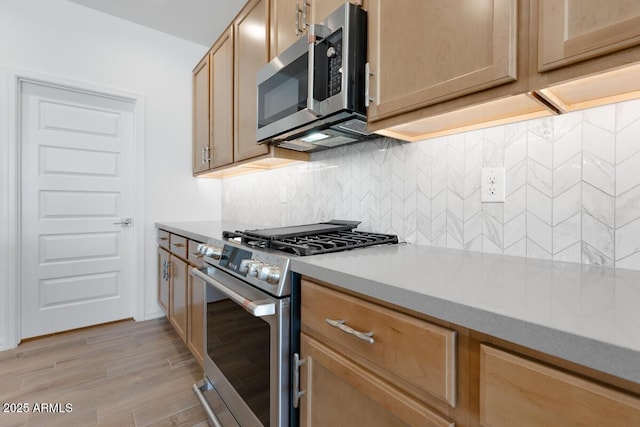 kitchen featuring tasteful backsplash, stainless steel appliances, light wood finished floors, and light countertops
