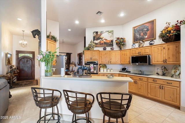 kitchen with appliances with stainless steel finishes, hanging light fixtures, a kitchen breakfast bar, kitchen peninsula, and a chandelier