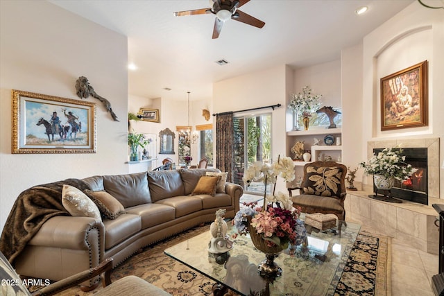 living room featuring a tiled fireplace and ceiling fan with notable chandelier