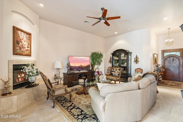 living room with a tiled fireplace, ceiling fan with notable chandelier, and light tile patterned floors