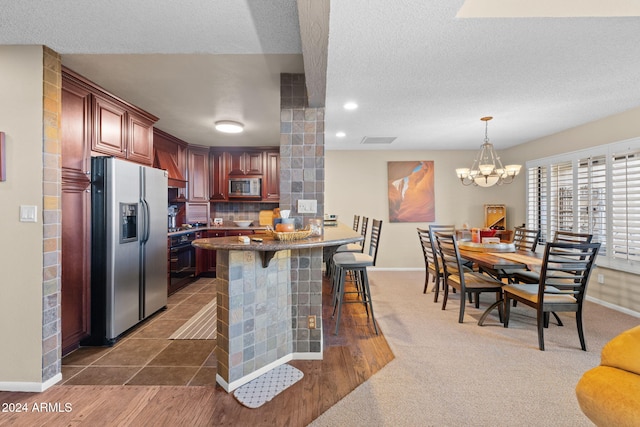 kitchen featuring a breakfast bar area, appliances with stainless steel finishes, a textured ceiling, decorative backsplash, and kitchen peninsula