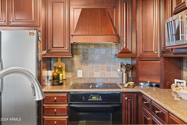 kitchen with premium range hood, tasteful backsplash, light stone counters, and black appliances