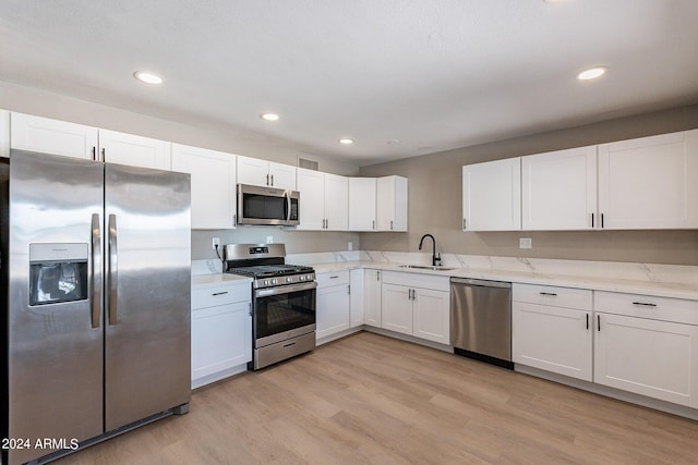 kitchen featuring sink, light wood-type flooring, light stone counters, white cabinetry, and stainless steel appliances