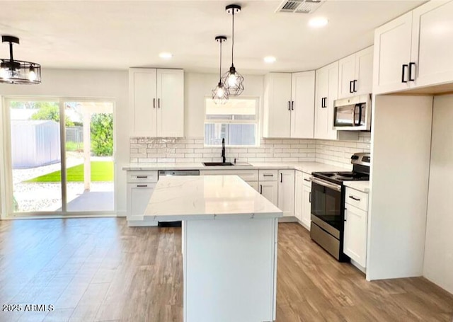 kitchen featuring decorative light fixtures, white cabinetry, a center island, and appliances with stainless steel finishes