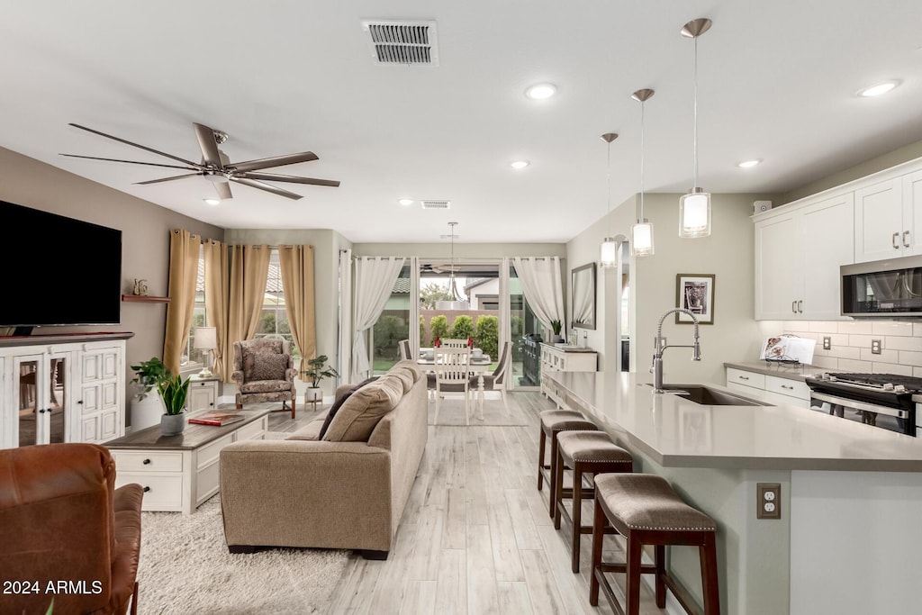 living room with light wood-type flooring, ceiling fan, and sink