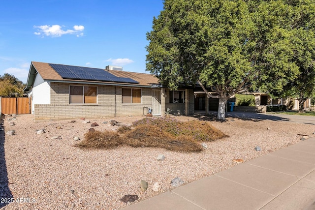 ranch-style home featuring roof mounted solar panels, brick siding, and fence