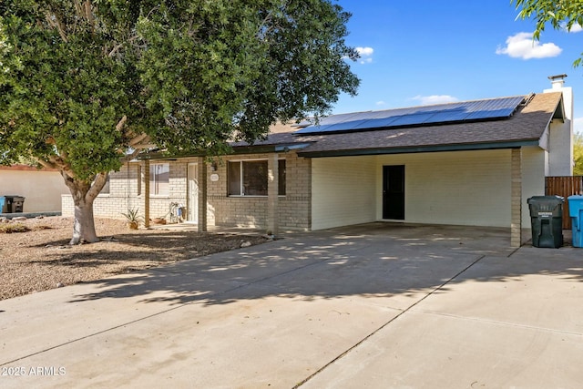 view of front of home featuring an attached carport, brick siding, driveway, and solar panels