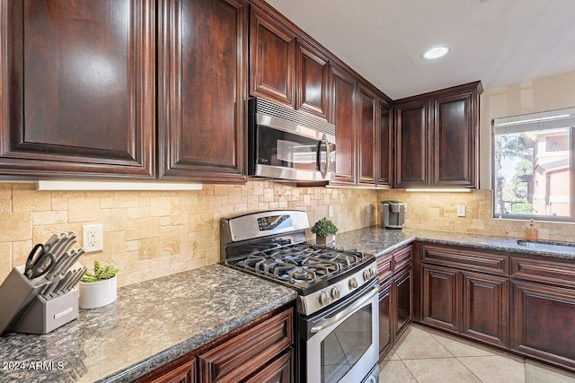 kitchen with backsplash, light tile patterned floors, stainless steel appliances, and dark stone counters