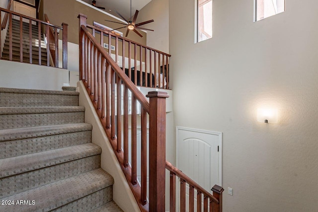 stairway featuring ceiling fan and a towering ceiling