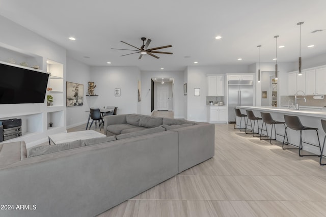 living room with built in shelves, ceiling fan, and sink