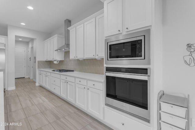 kitchen featuring appliances with stainless steel finishes, tasteful backsplash, white cabinetry, and wall chimney range hood