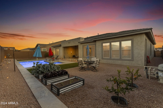 back house at dusk featuring a patio and a fenced in pool