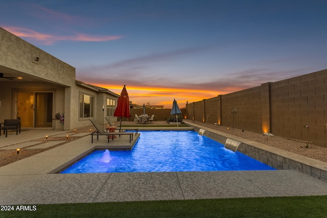 pool at dusk with a patio area and pool water feature