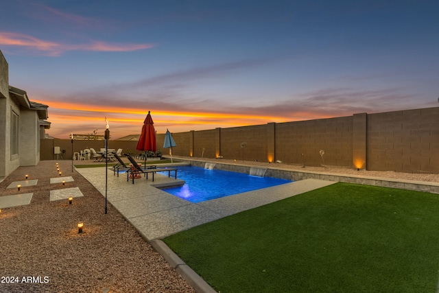 pool at dusk with pool water feature and a patio area