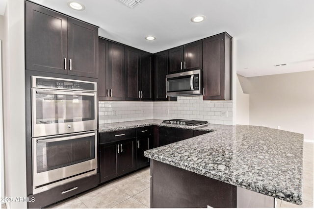 kitchen with light tile patterned floors, light stone counters, a peninsula, decorative backsplash, and appliances with stainless steel finishes